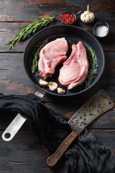 Raw pork steak on the bone in frying grill pan with butcher knife or cleaver and ingedients for grill side top view vertical on old wood brown dark table planks.