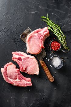 Organic Pork meat chop over american classic butcher knife or cleaver with spices and rosemary and red pepper on black slate table top view. space for text in corner.