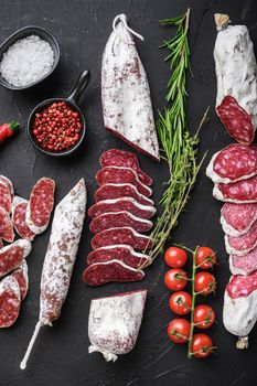 Set of various spanish dry cured salami sausages slices and whole cuts on balck background, top view.