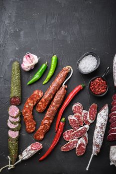 Set of various spanish dry cured salami sausages slices and whole cuts on black textured background, topview with space for text.