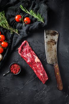 Organic machete or hanger butcher steak, near butcher knife with pink pepper and rosemary. Black background. Top view. Vertical.