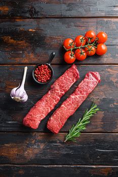 Raw marbled beef steak with pink pepper and rosemary. cut of beef called the denver steak or organic top blade wuth herbs on old dark wooden table surface top view space for text vertical.