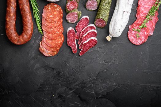 Set of dry cured salami, spanish sausages, slices and cuts on black background, top view with copy space.