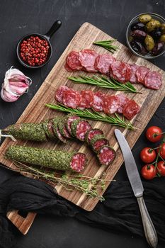 Spanish fuet salami sausage slices on black textured background, topview.