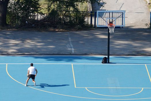 Varna, Bulgaria - August, 22, 2020: young man training with a ball on an outdoor basketball court, view from above
