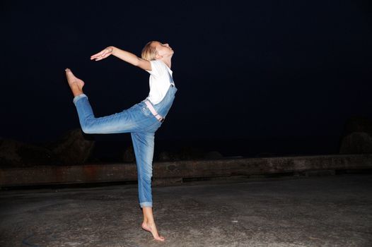 barefoot teenage girl dancing ballet on an empty pier at night.