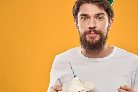 Handsome man with a beard and in a cap celebrating a birthday party yellow background. High quality photo