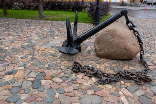 An old black anchor lies on the cobblestones.