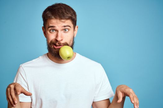 An energetic man with a green apple on a blue background gestures with his hands Copy Space emotions. High quality photo