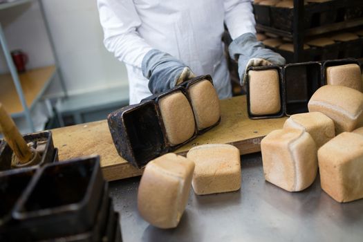 Close-up. Baker dumps freshly prepared bread out of molds on the table.