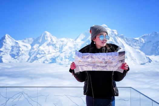 Young female tourist looking map at the Schilthorn in Switzerland with a magnificent panoramic view of the Swiss Skyline.