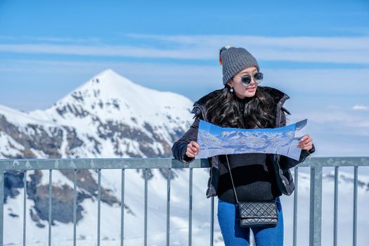 Young female tourist looking map at the Schilthorn in Switzerland with a magnificent panoramic view of the Swiss Skyline.