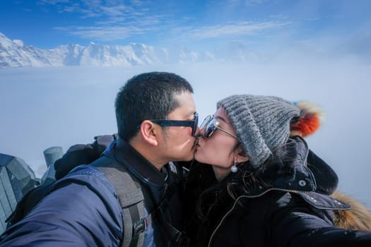 Young Couple Tourists selfie kiss with mobile phone near view of the Swiss Skyline from Schilthorn, Switzerland