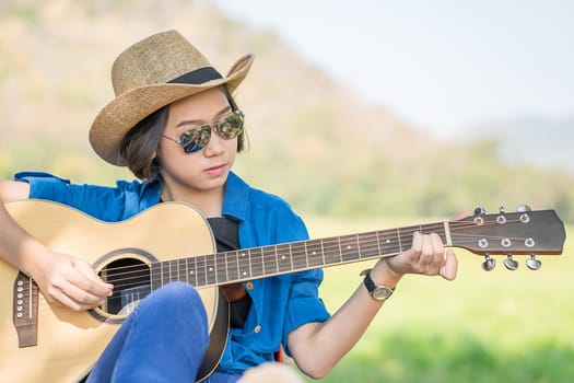 Close up young asian women short hair wear hat and sunglasses playing guitar in countryside Thailand