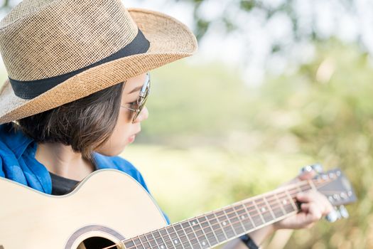 Close up young asian women short hair wear hat and sunglasses playing guitar in countryside Thailand