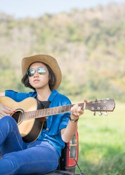 Young asian women short hair wear hat and sunglasses playing guitar ,sit on pickup truck in countryside Thailand