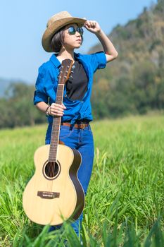 Young asian woman short hair wear hat  and carry her guitar  in grass field countryside Thailand