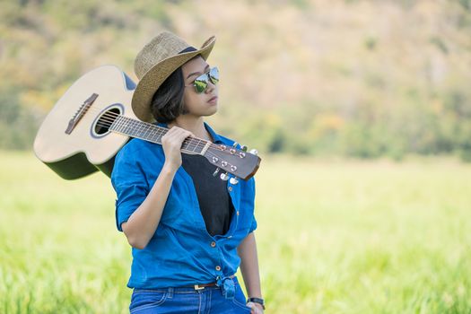 Young asian woman short hair wear hat  and carry her guitar  in grass field countryside Thailand