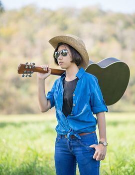 Young asian woman short hair wear hat  and carry her guitar  in grass field countryside Thailand