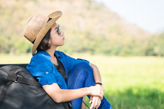 Young asian women short hair wear hat and sunglasses carry her guitar bag ,sit on pickup truck in countryside Thailand