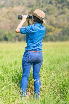 Young asian woman short hair wear hat and hold binocular in grass field countryside Thailand