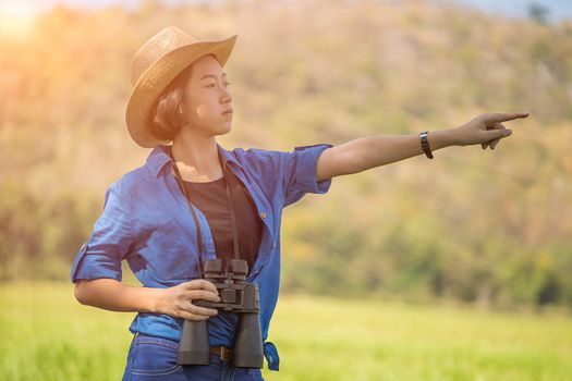 Young asian woman short hair wear hat and hold binocular in grass field countryside Thailand