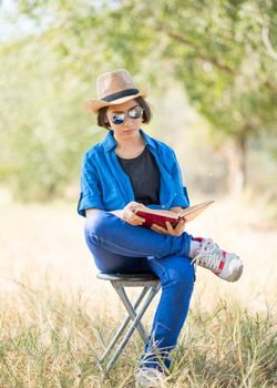 Young asian women short hair wear hat and sunglasses read a book ,sit on chair in countryside Thailand