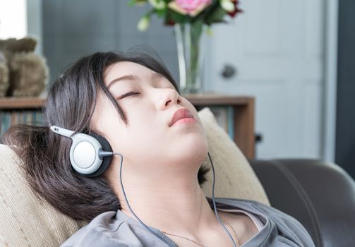 Close up beautiful young asian woman short hair listening music on the couch at home