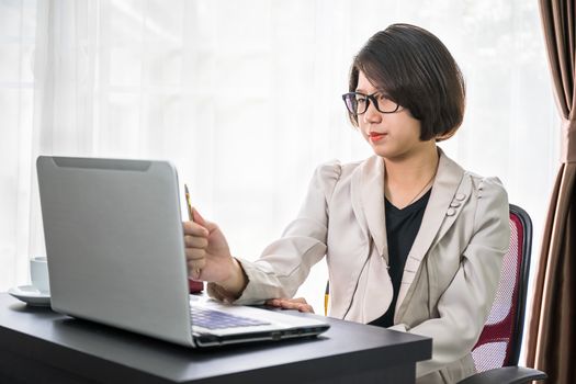 Young asian woman short hair in smart casual wear working on laptop while sitting near window in home office