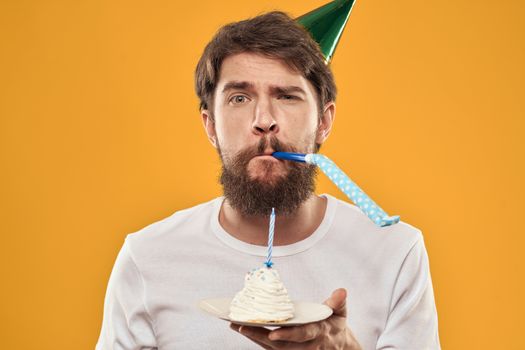 Handsome man with a beard and in a cap celebrating a birthday party yellow background. High quality photo