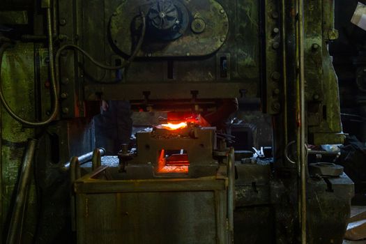 Close-up picture of fresh forged hot steel workpieces after press forming in dirty dark factory. Selective focus on foreground.