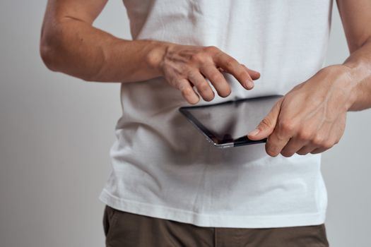 Tablet with a touch screen on a light background male hands white t-shirt cropped view. High quality photo