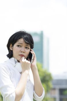 Worrying asian woman making phone call in garden. Blurry building background.