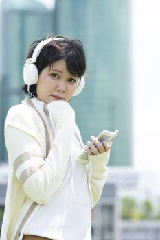 Happy asian woman listening to music on mobile phone. Blurry building background.