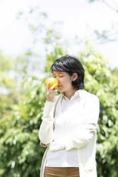 Happy asian woman holding orange in garden. Smiling people with blurry background.