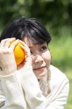 Happy asian woman holding orange in garden. Smiling people with blurry background.