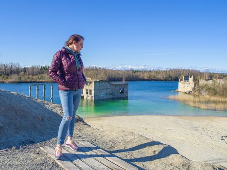 Hiker on mountain top. Woman is standing with an Abandoned Quarry and water on the background. Scenic View Of Land Against Clear Blue Sky. Panoramic View.