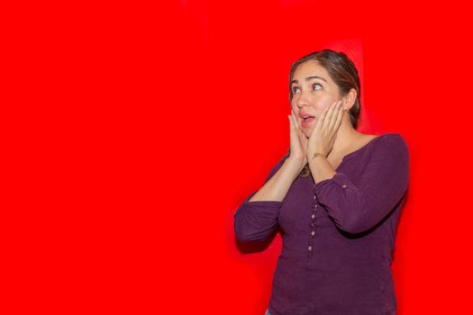 Image of a 30 year old caucasian woman with long brown hair looking at the camera and pointing with her fingers in the copy space isolated on red background