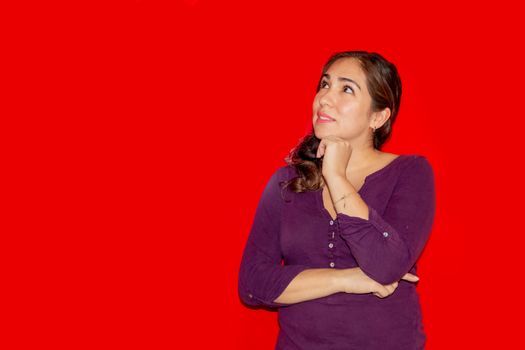Image of a 30 year old caucasian woman with long brown hair looking at the camera and pointing with her fingers in the copy space isolated on red background