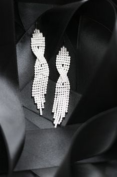 Luxury diamond earrings on black silk ribbon as background, jewelry and fashion brands