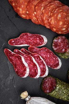 Set of dry cured salami, spanish sausages, slices and cuts on black background, top view.