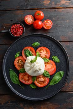 Handmade burrata cheese served with fresh tomatoes and basil leaves traditional italian Salad vertical top view. wood table old rustic