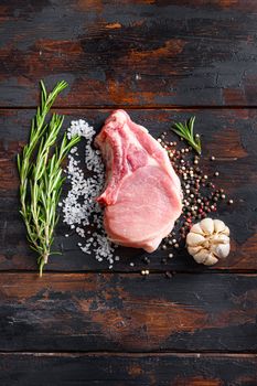 Raw meat on dark wood rustic background. Bio organic farm pork steak with herbs and spices. Cooking meat. Copy space. Top view vertical space for price or text.