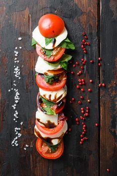 Concept Top view of fresh italian caprese salad with tomatoes, mozzarella, green basil sliced on old kitchen table top view vertical.