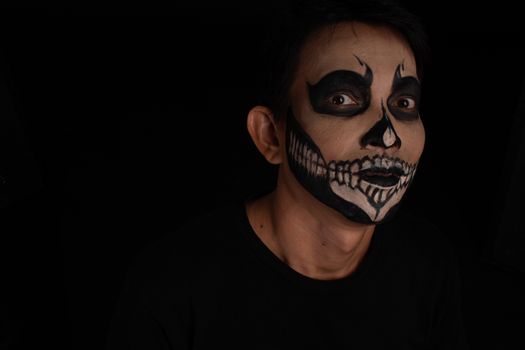 Southeast asian man with skull face makeup on black background, portrait photography