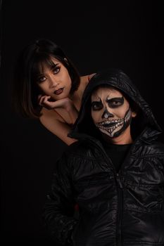 Southeast asian man with skull face makeup and woman on black background, portrait photography