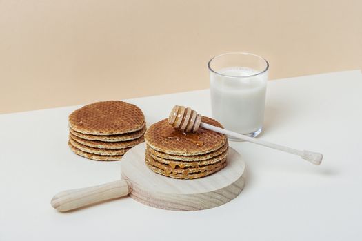 Honey dipper pouring honey over a pile of waffles on a wooden tray. Copy space