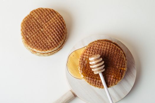 Honey dipper pouring honey over a pile of waffles on a wooden tray. Top view.