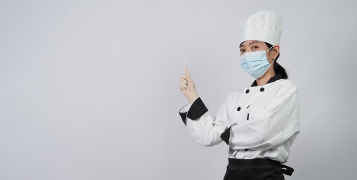 Asian woman chef in white color uniform with hygienic such as medical face mask and rubber hand glove for prevent or protect covid-19 or coronavirus pandemic. Studio shot and copy space.