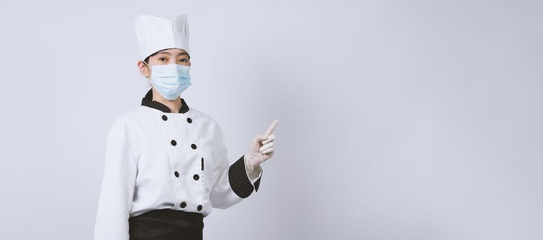 Asian woman chef in white color uniform with hygienic such as medical face mask and rubber hand glove for prevent or protect covid-19 or coronavirus pandemic. Studio shot and copy space.